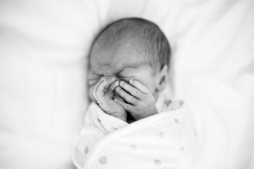 newborn baby with his hands in front of his face